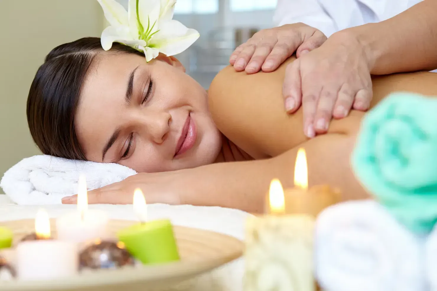Relaxed spa massage with candles, towels, and a white flower resting on a woman’s hair