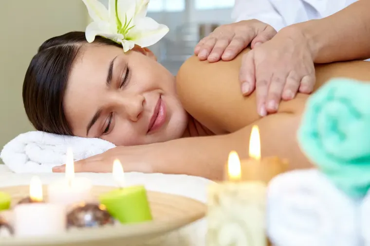 Person relaxing face down during a spa massage with candles, towels, and a white flower in their hair