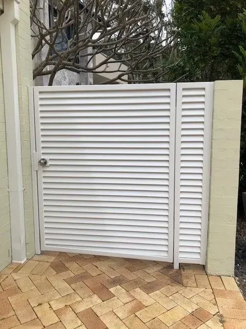 A White Gate is Sitting on Top of a Brick Driveway — Sunshine Gates in Kunda Park, QLD