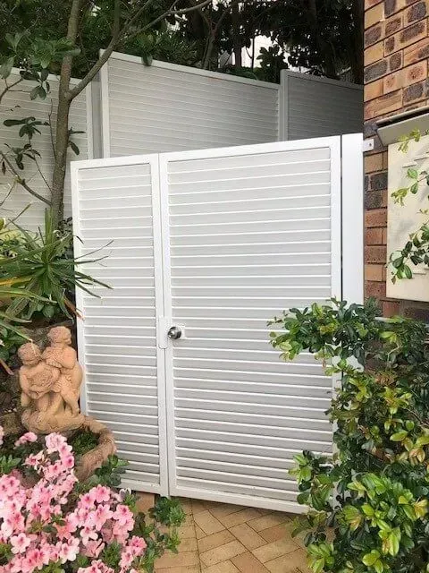 A White Gate is Sitting Next to a Brick Building in a Garden — Sunshine Gates in Kunda Park, QLD