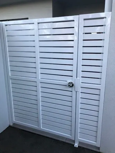 A White Gate With a Door is Sitting Next to a Wall — Sunshine Gates in Kunda Park, QLD