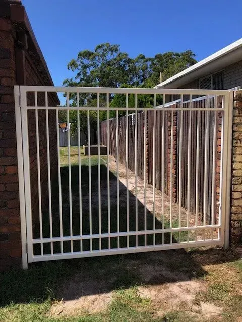 A White Gate is Sitting Next to a Brick Wall — Sunshine Gates in Kunda Park, QLD