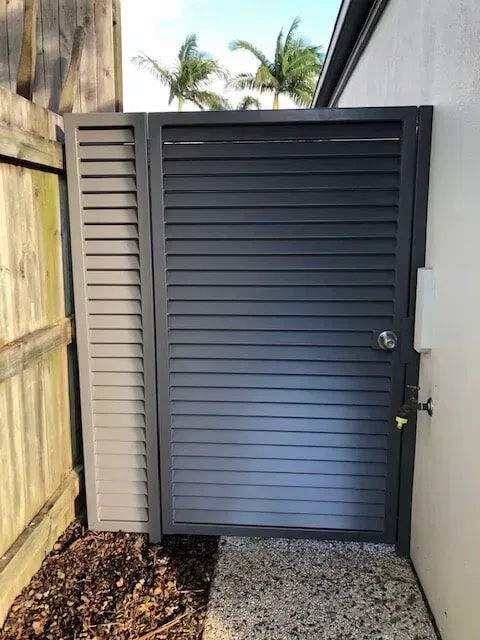 A Black Gate is Sitting Next to a Wooden Fence— Sunshine Gates in Kunda Park, QLD