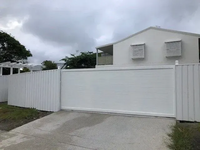 A White Fence Surrounds a White House With a Sliding Gate — Sunshine Gates in Kunda Park, QLD