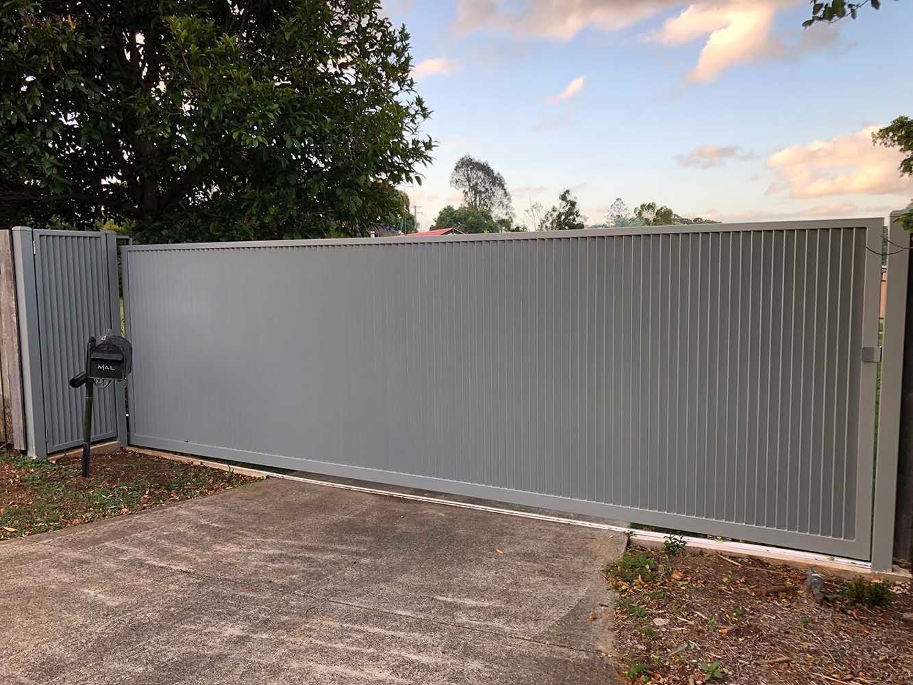 A Gray Sliding Gate is Sitting on Top of a Concrete Driveway Next to a Mailbox — Sunshine Gates in Kunda Park, QLD
