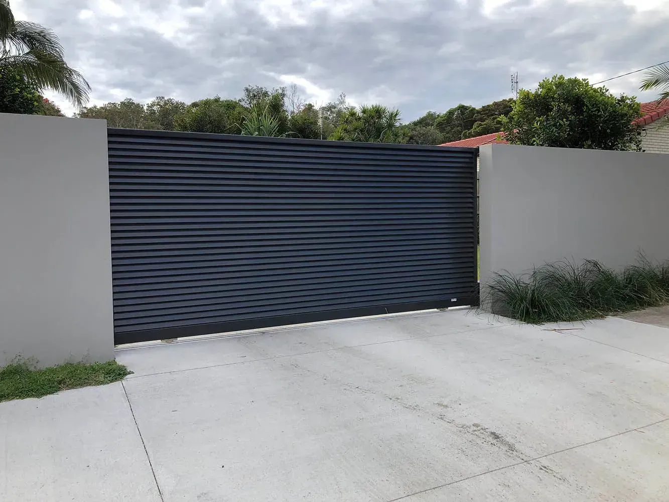 A Black Garage Door is Sitting Next to a White Wall — Sunshine Gates in Kunda Park, QLD