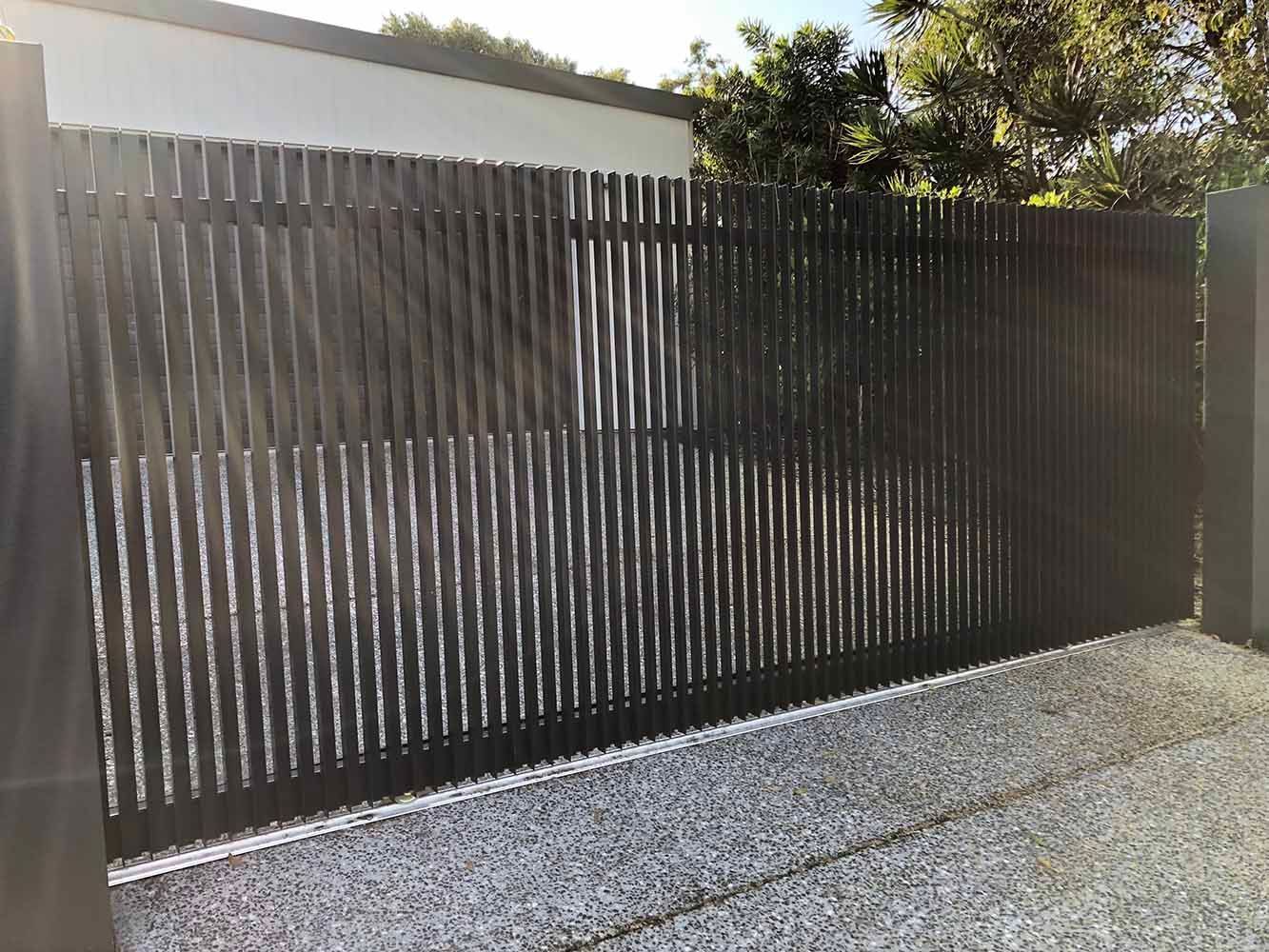 A Black Sliding Gate is Sitting on Top of a Gravel Driveway — Sunshine Gates in Kunda Park, QLD