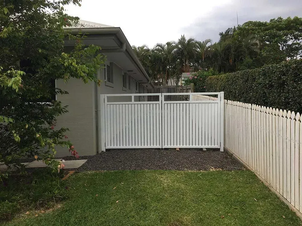 A White Fence Surrounds a Lush Green Yard in Front of a House — Sunshine Gates in Kunda Park, QLD