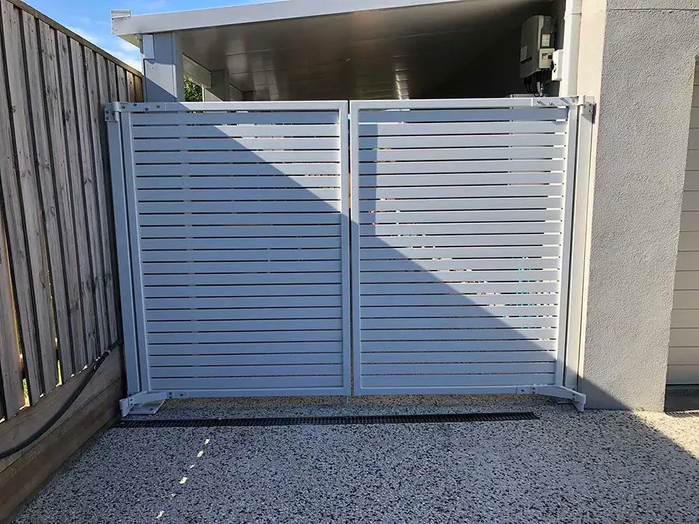 A White Gate is Sitting Next to a Wooden Fence — Sunshine Gates in Kunda Park, QLD