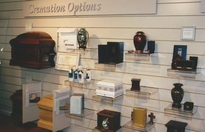Display of cremation urns and memorial containers on shelves under a “Cremation Options” sign