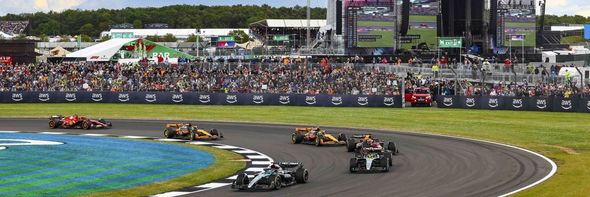 Race cars speed around a wet track with a crowd watching from the grandstands.