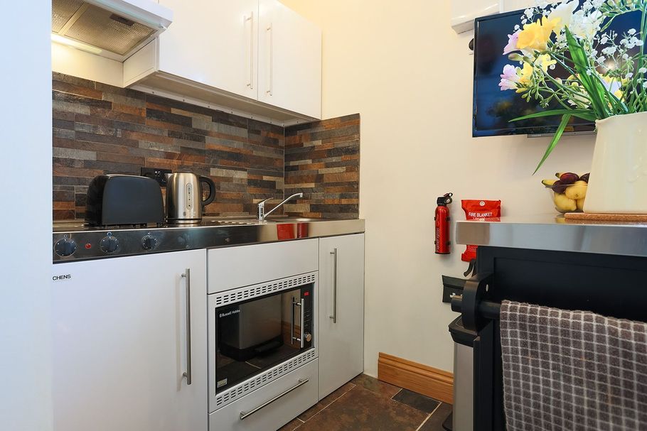 Compact kitchen with white cabinets, brick backsplash, oven, toaster, and flowers on a shelf