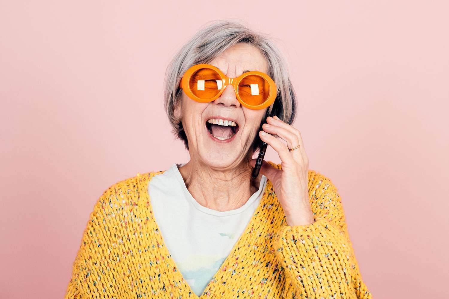 An elderly woman wearing sunglasses is talking on a cell phone.