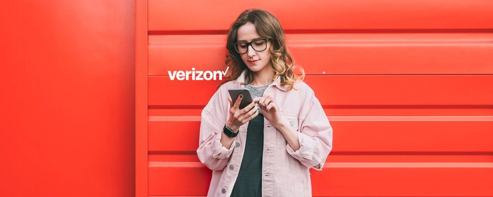 A woman is standing in front of a red wall looking at her cell phone.