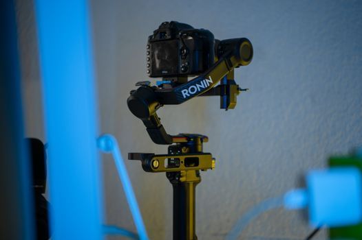 Cámara montada sobre un estabilizador negro en un trípode, iluminada con luz azul, en una habitación.