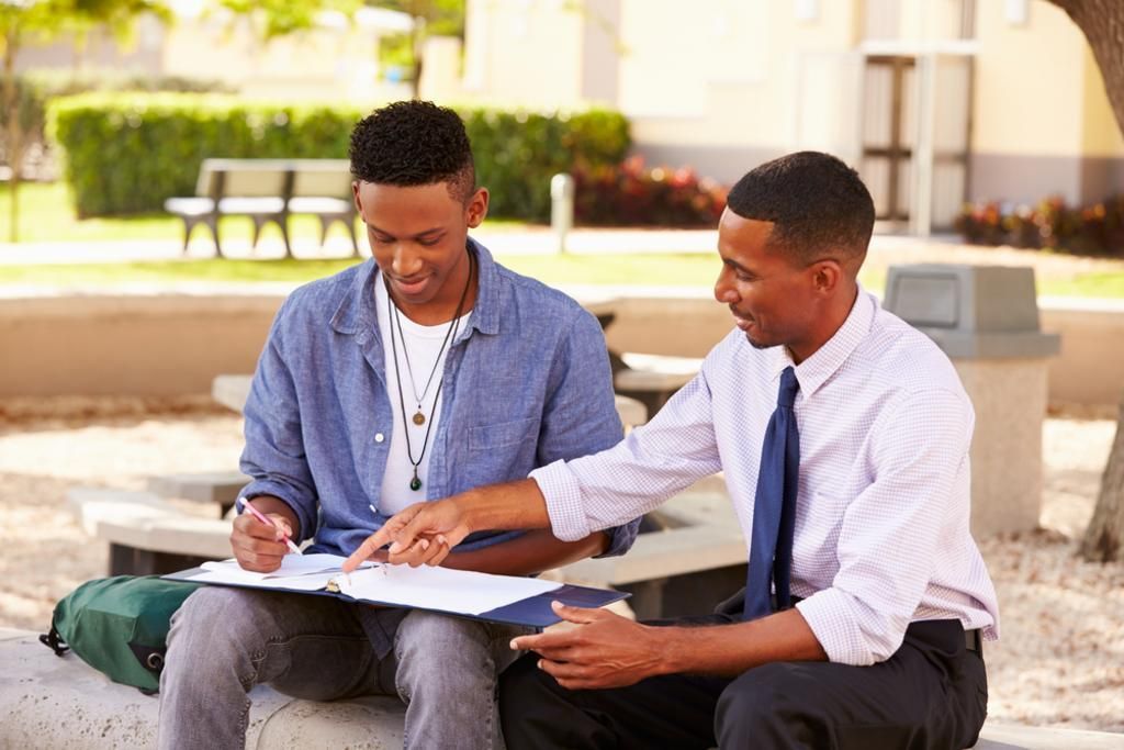 Two men are sitting on a bench looking at a clipboard.
