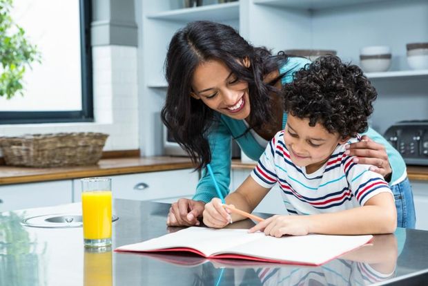 A woman is helping a young boy with his homework in the kitchen.