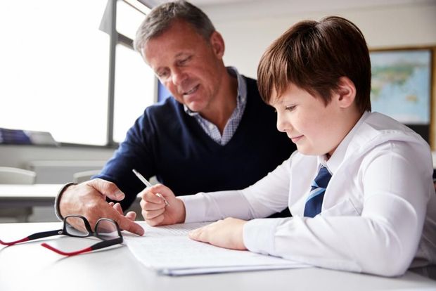 A man is helping a young boy with his homework in a classroom.