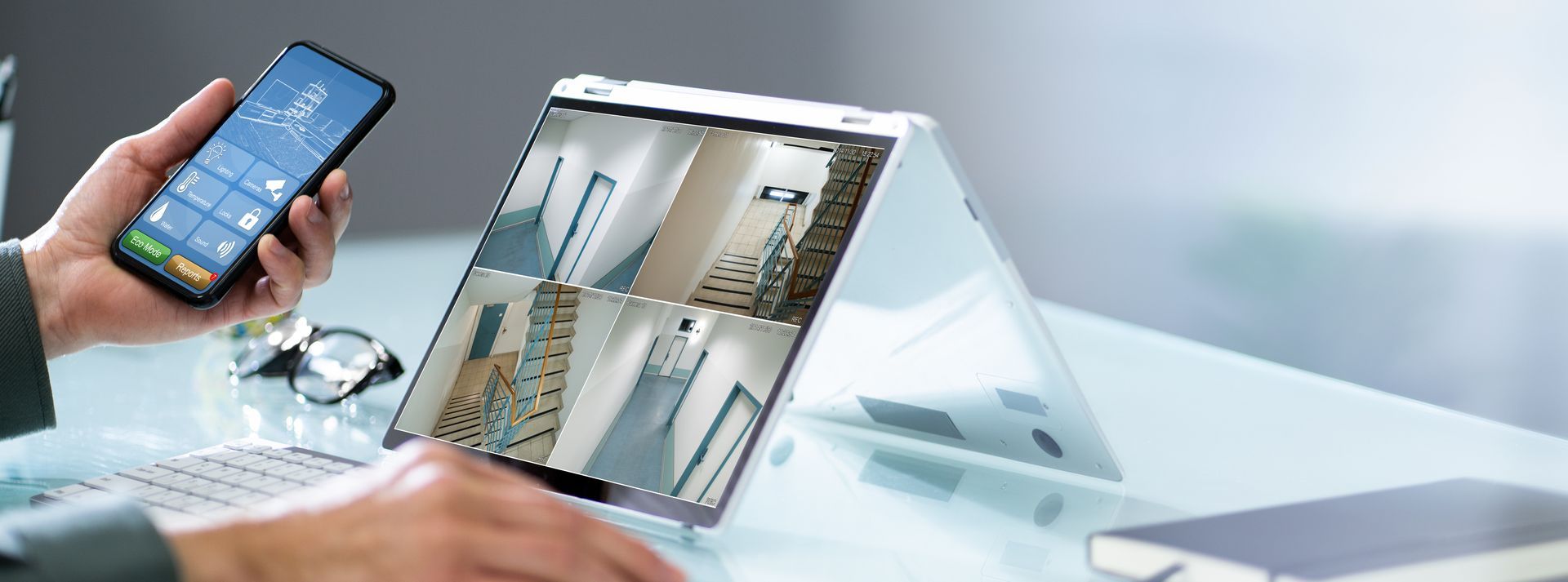 Hands holding a smartphone beside a tablet displaying a video call on a white desk