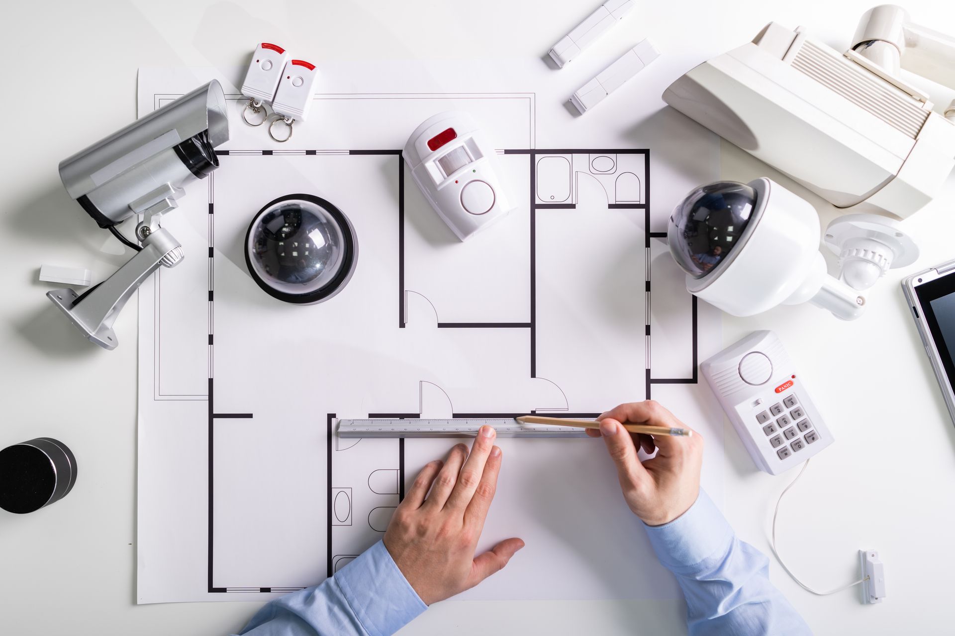 Architect drafting a floor plan with pen, ruler, and security cameras on a white desk