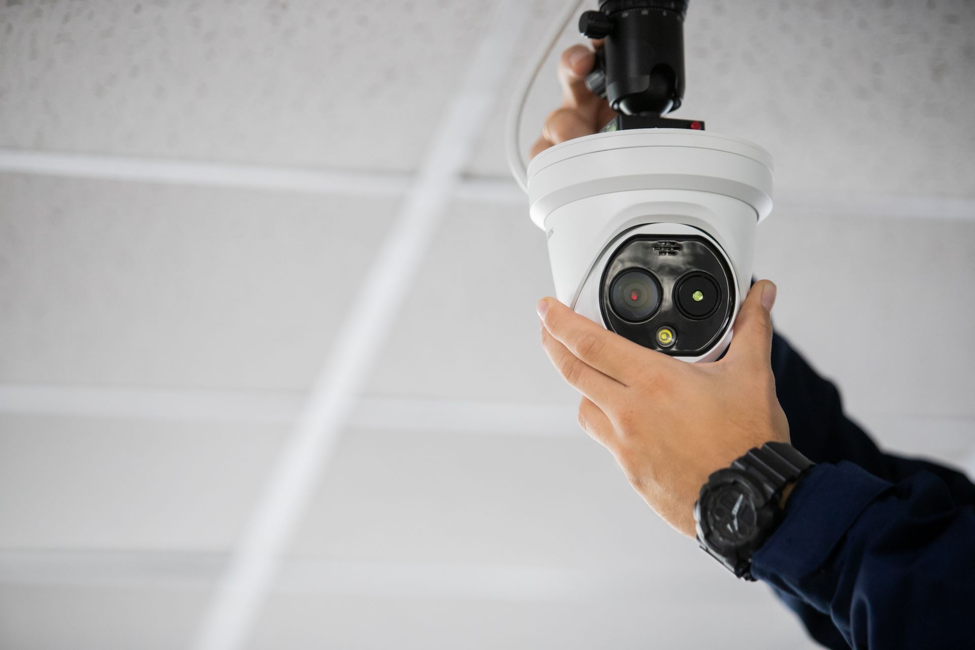 Person installing a white security camera on a ceiling