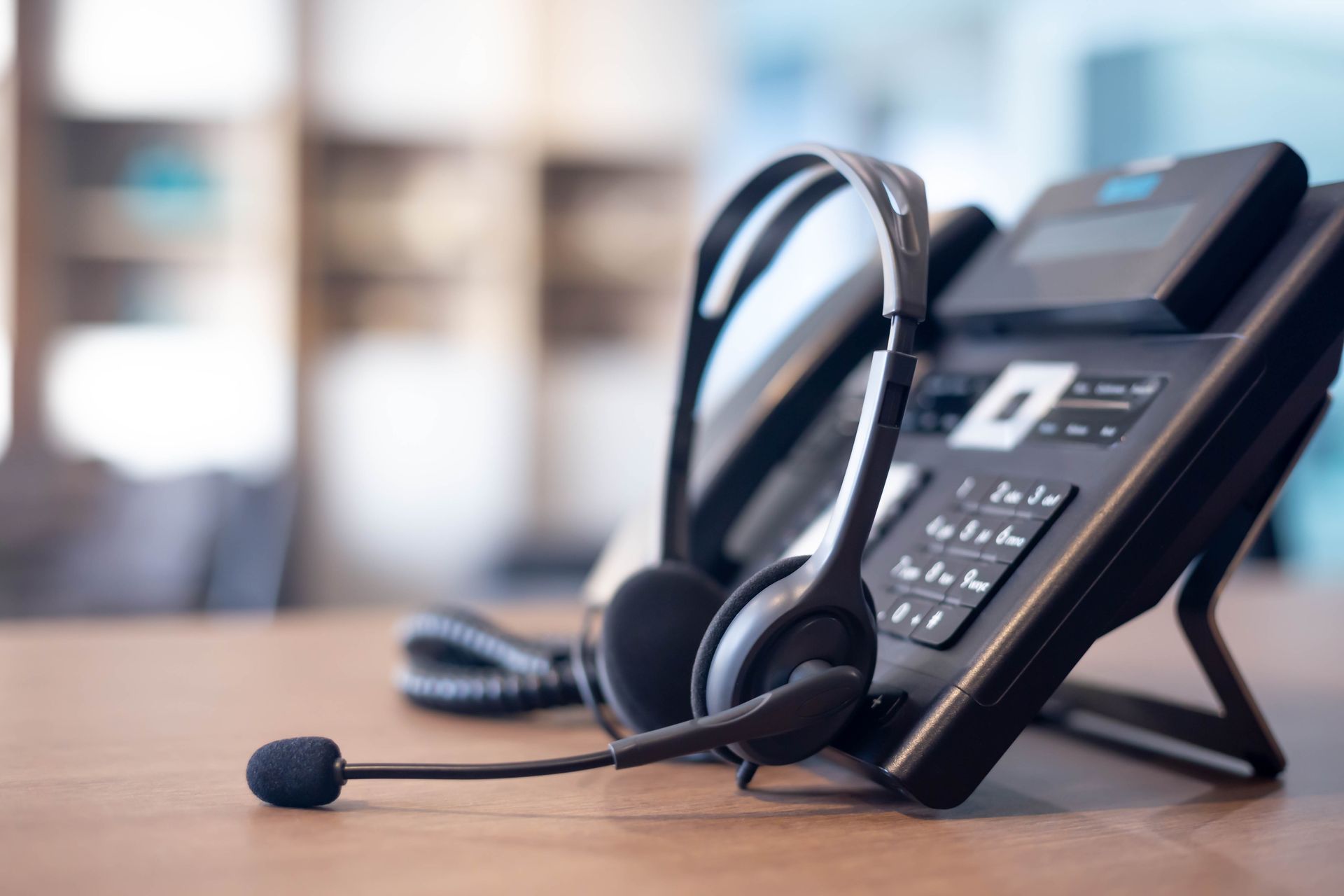 Office desk phone with headset resting on a wooden table
