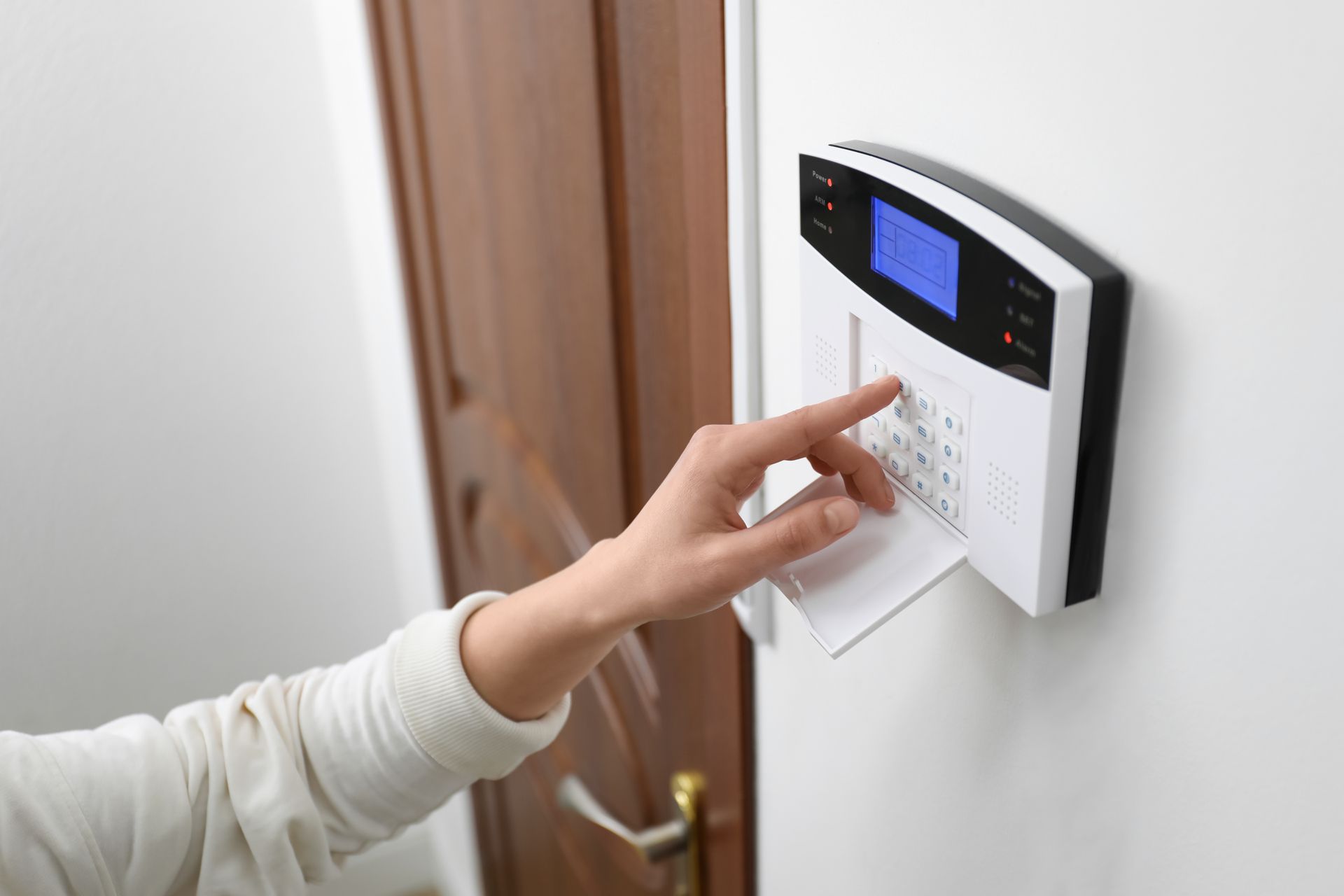Person entering a code on a wall-mounted home security keypad with blue display.