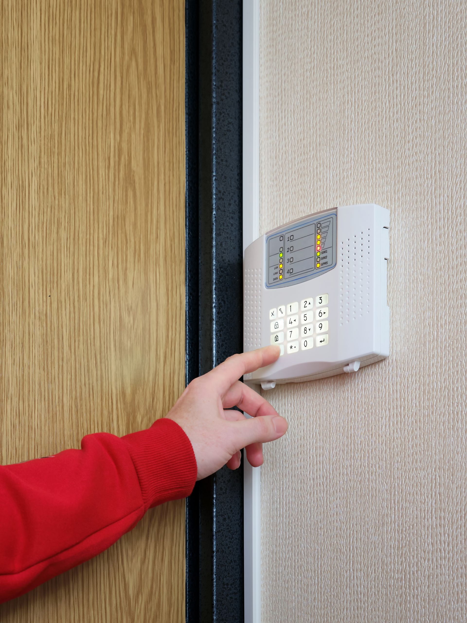 Hand pressing a wall-mounted security keypad beside a door.