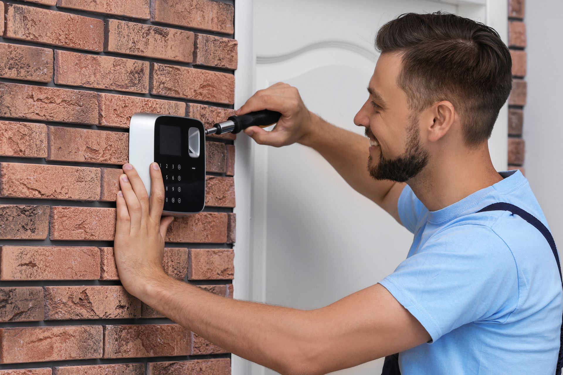 Technician installing a black wall-mounted security keypad on a brick wall