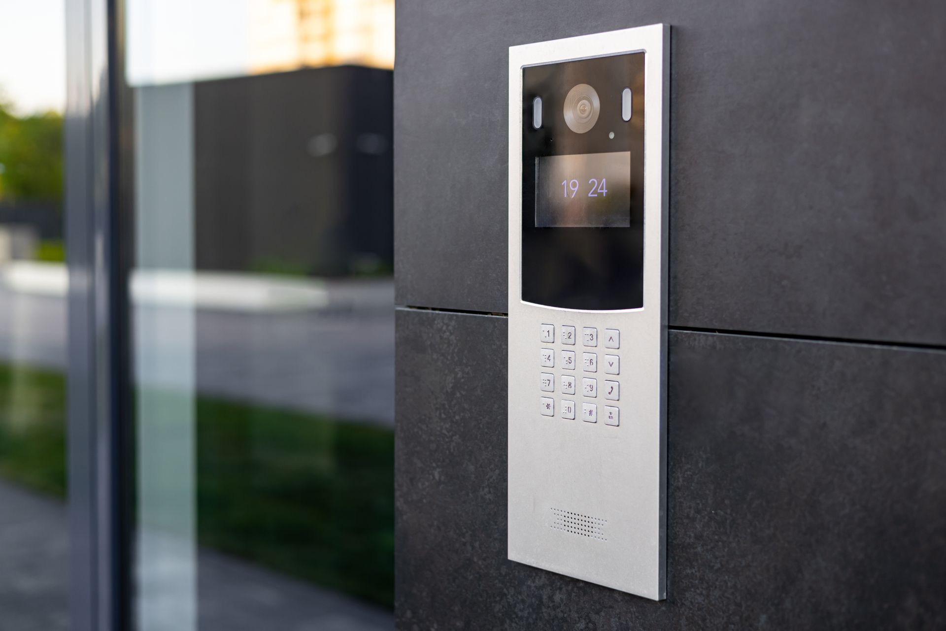 Silver intercom keypad on a dark exterior wall beside a glass entrance