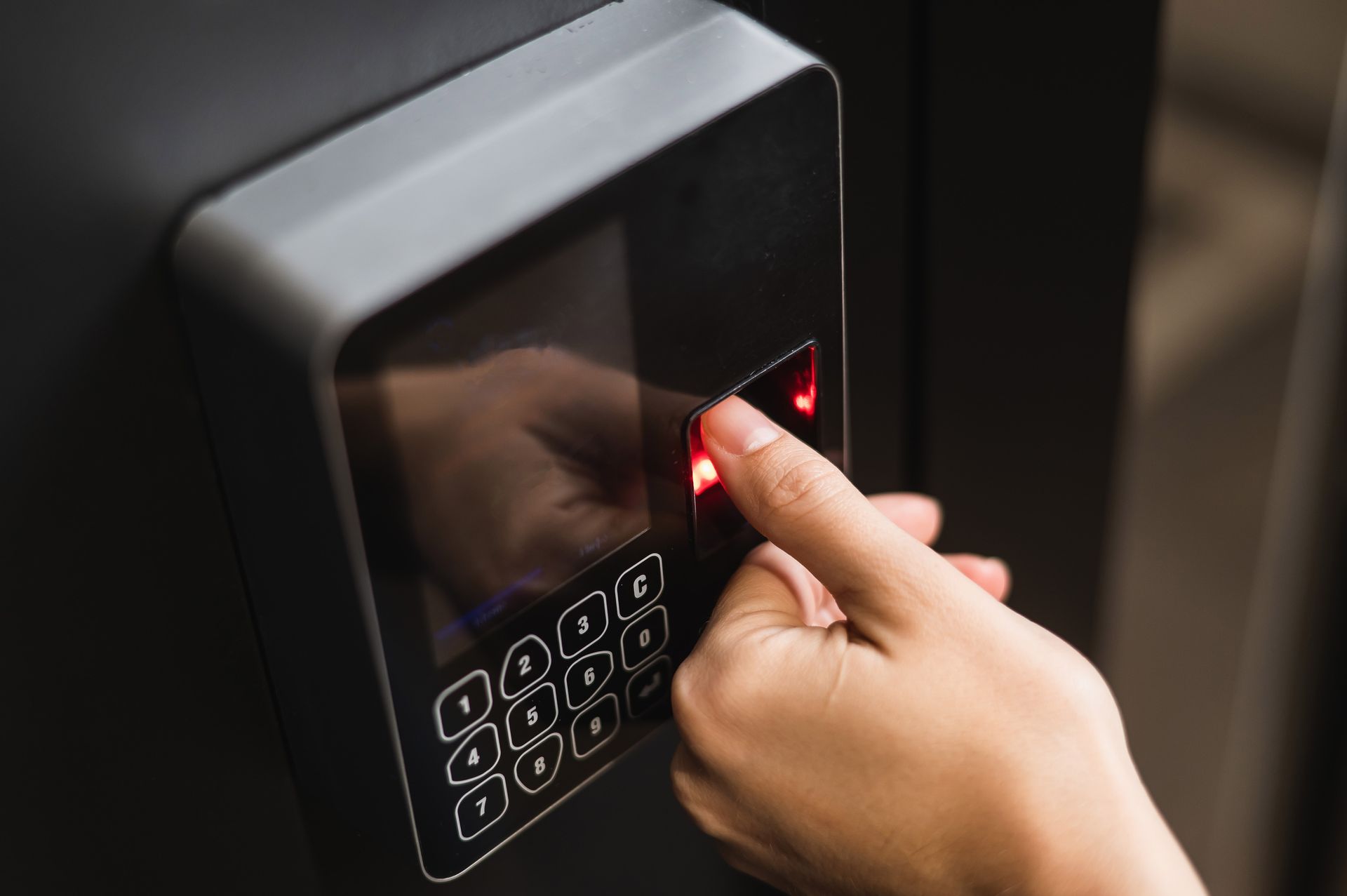 Hand pressing a lit code on a sleek black keypad access panel