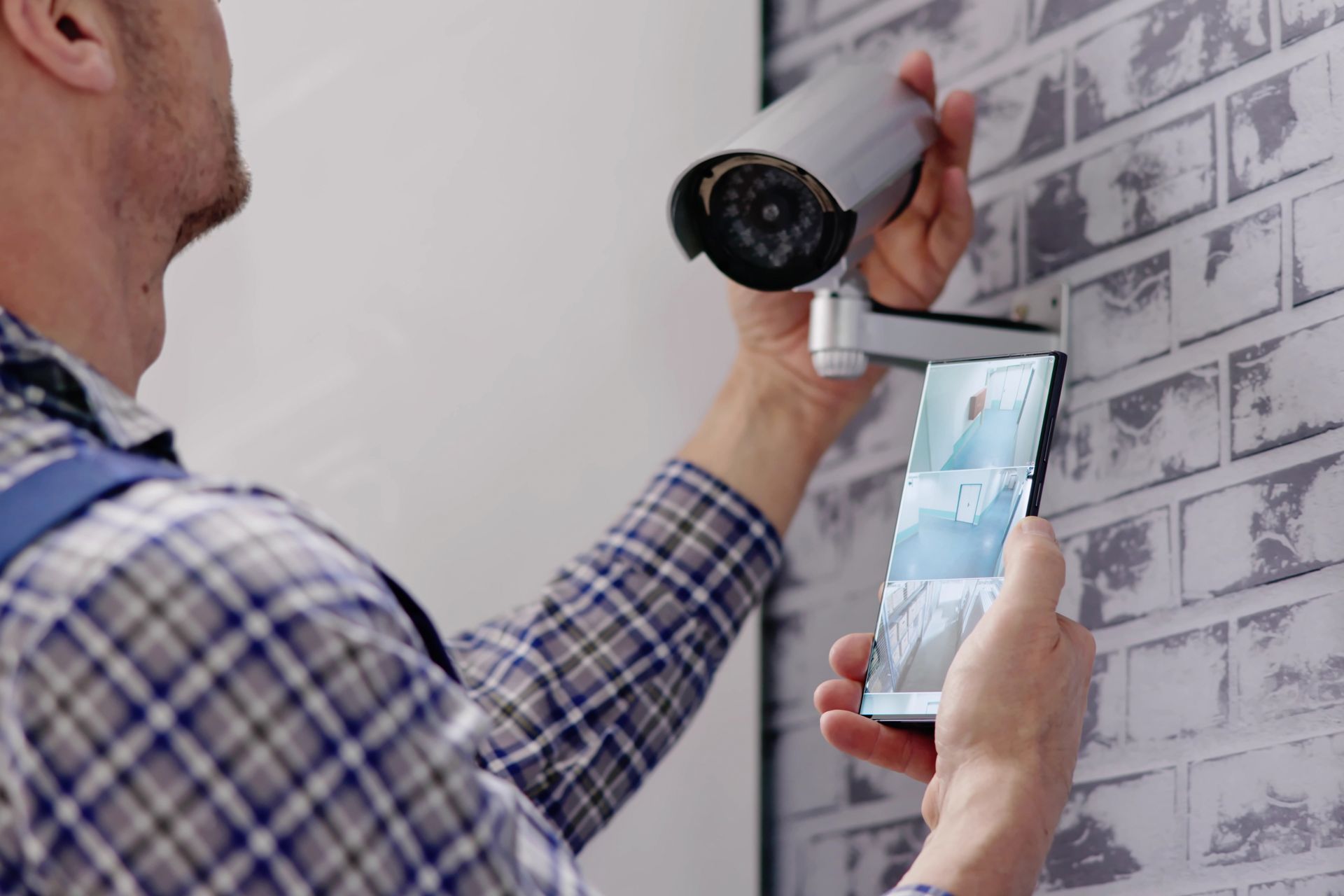 Person installing a white security camera while holding a smartphone against a wall