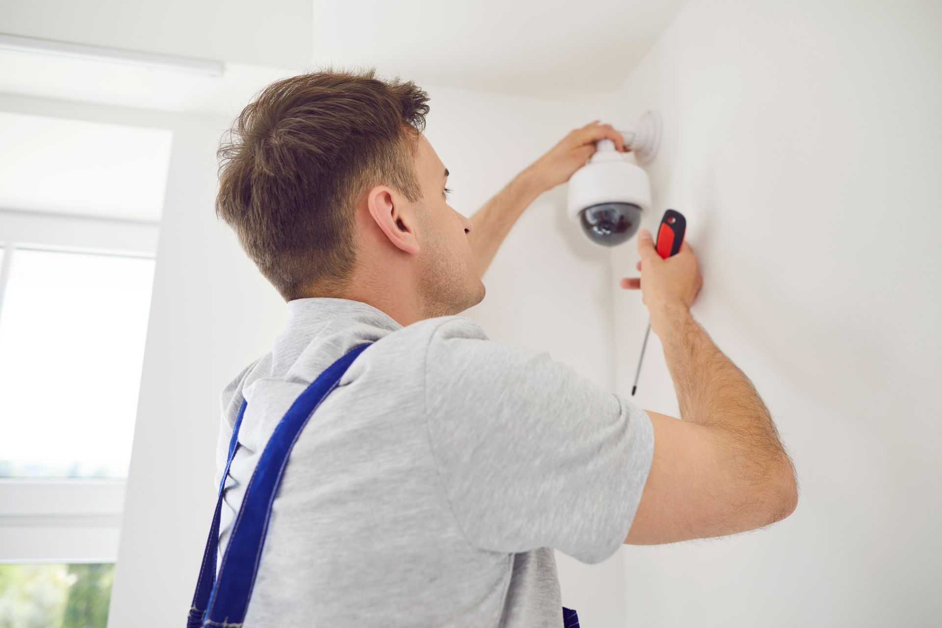 Person installing a white ceiling light fixture with a red screwdriver in a bright room