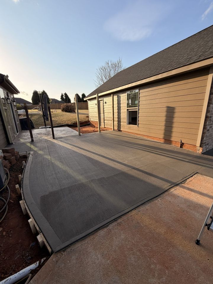 Concrete patio beside a brick house at sunset, with a gate and landscaped yard.