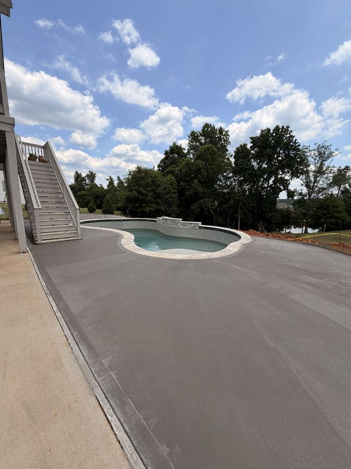Backyard pool with white slide, paved deck, and trees under a partly cloudy sky
