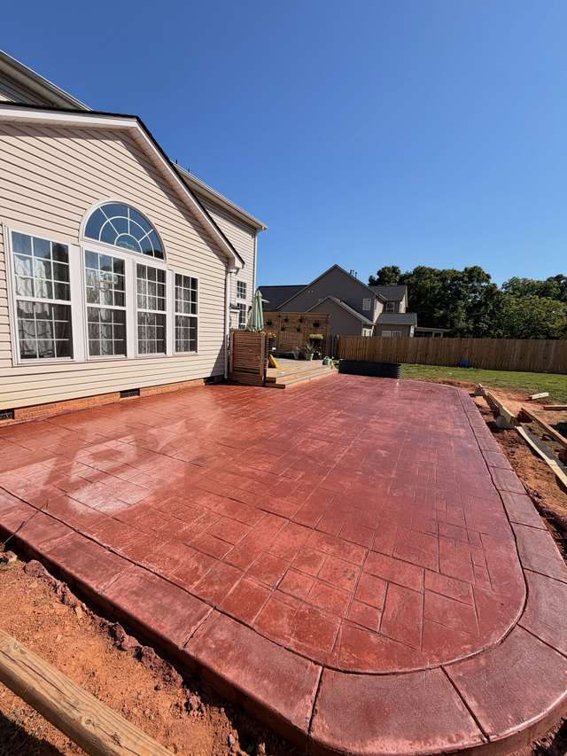 Red stamped concrete patio beside a house with large windows under a clear blue sky.