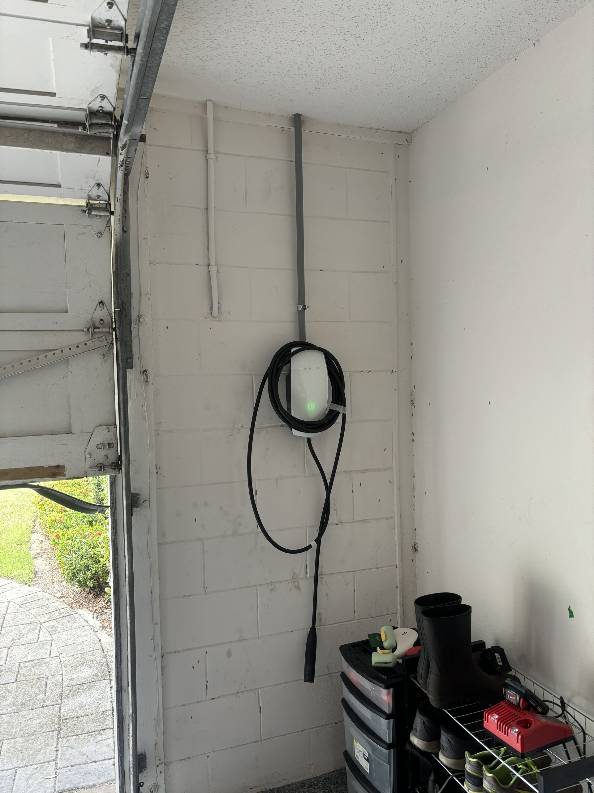 Garage wall with coiled black hose, shelves, and a partially open door with daylight outside