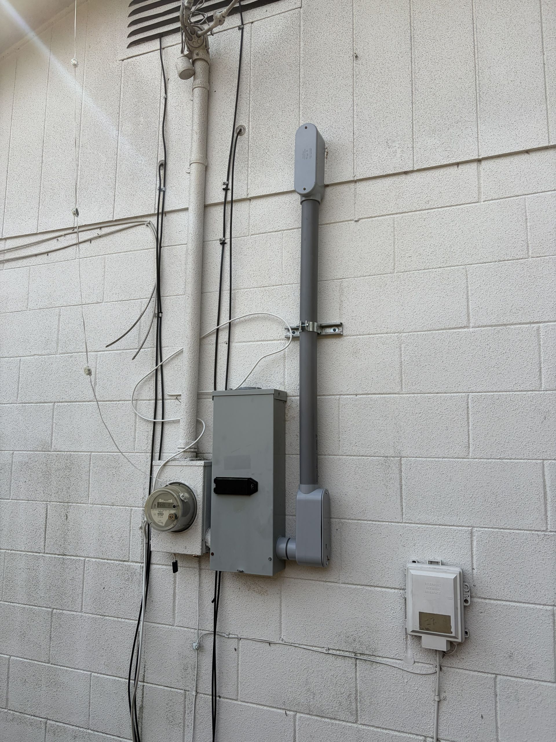 Gray utility meter and electrical box mounted on a cinder block wall with exposed conduit wires