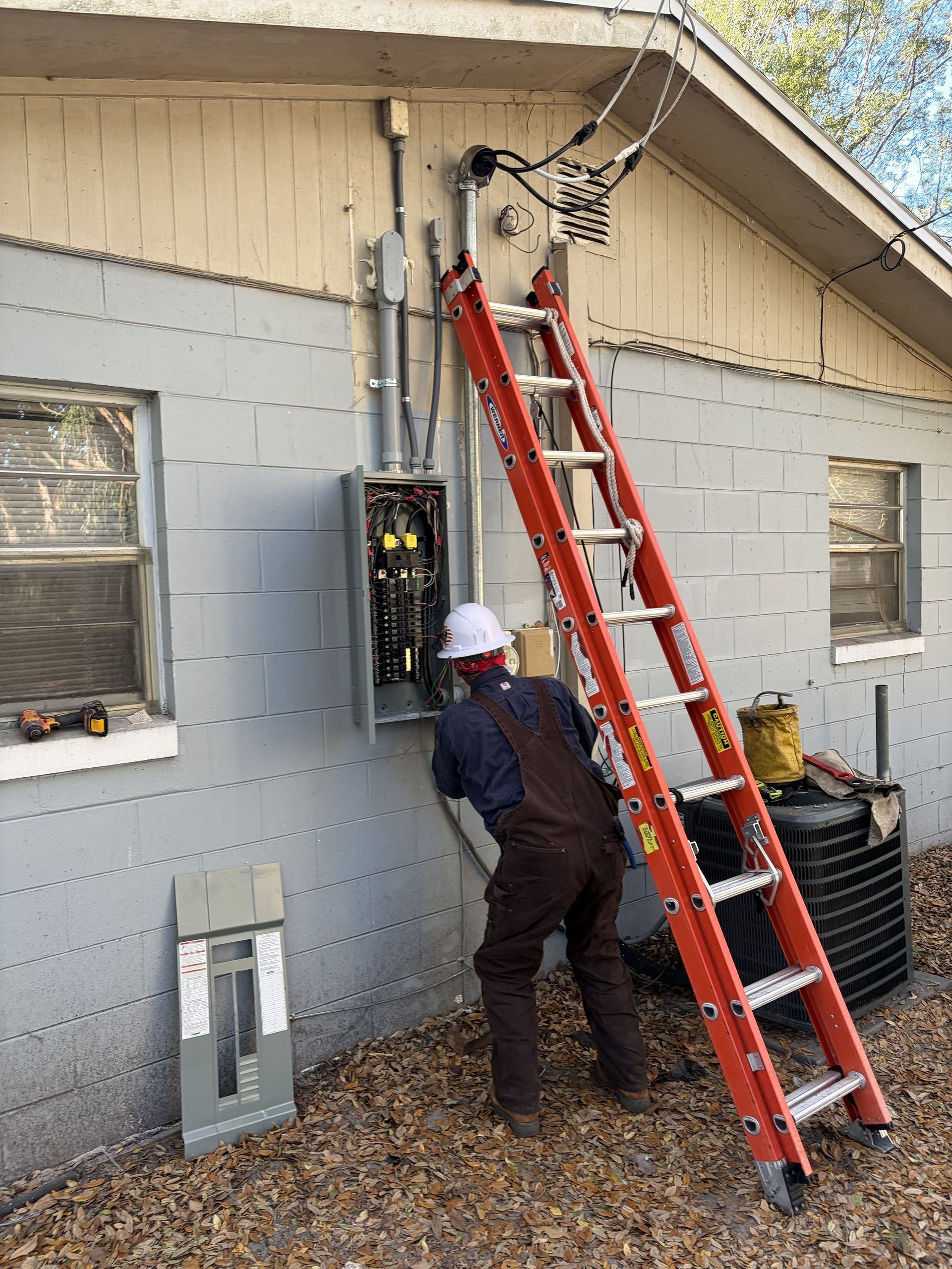 Worker inspecting electrical panel beside house with red ladder leaning against the wall
