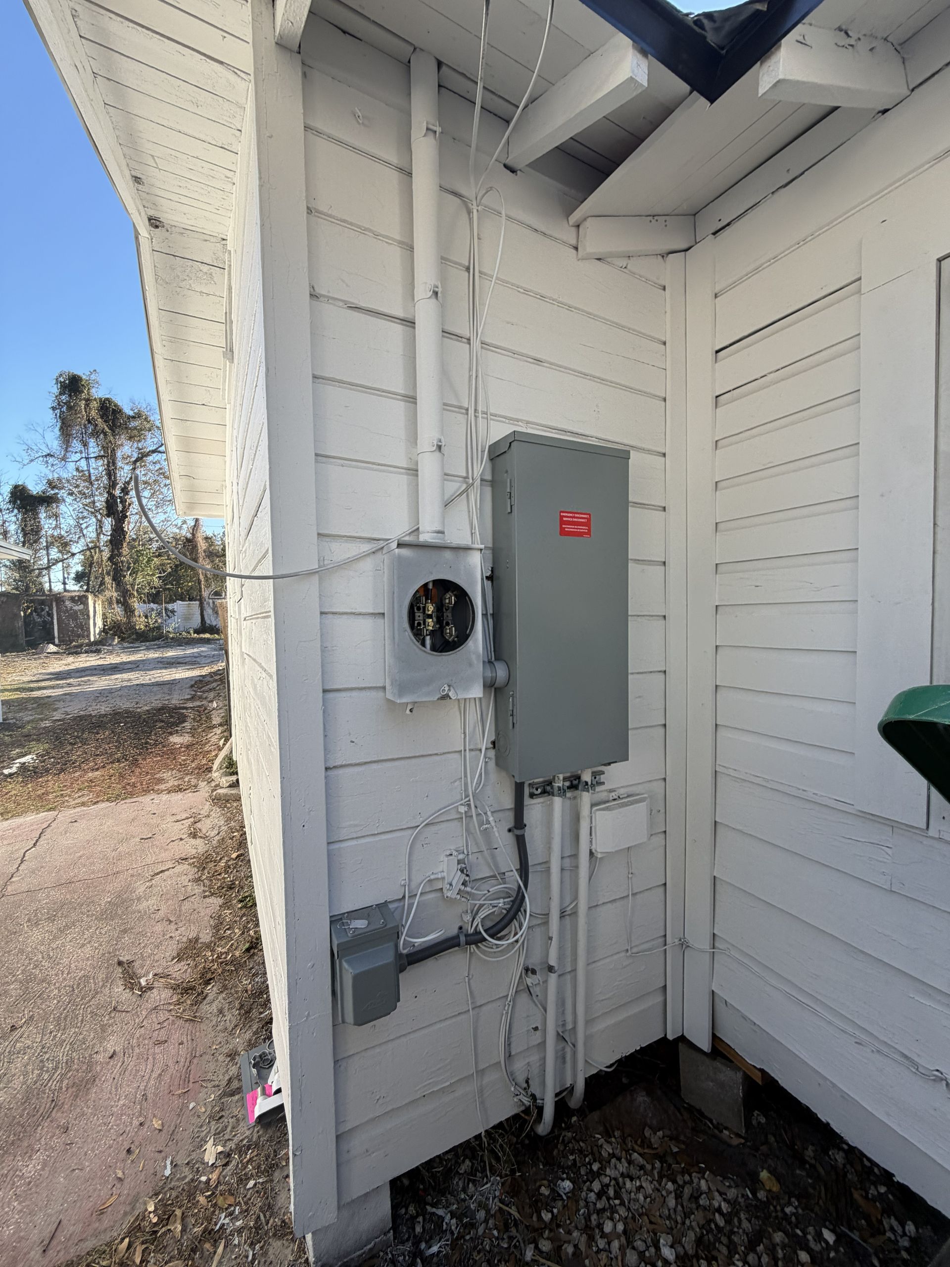 Electrical meter and service panel mounted on the exterior wall of a white house.