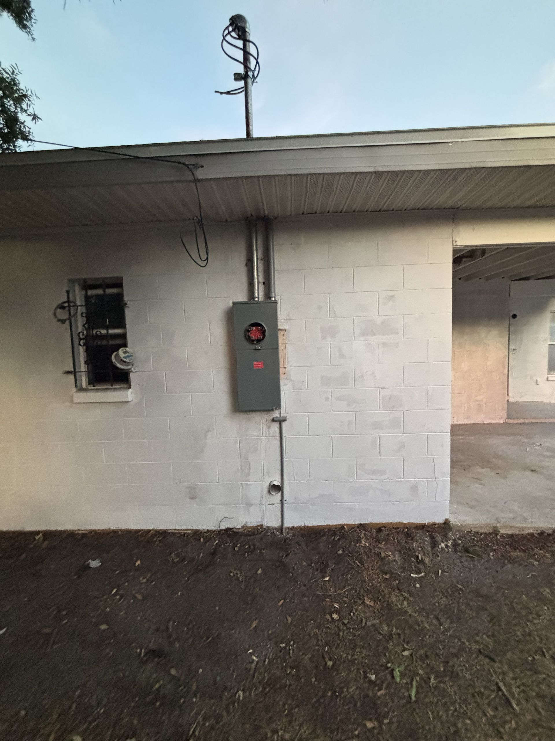 White brick wall with an electrical panel and wiring under a roof overhang.