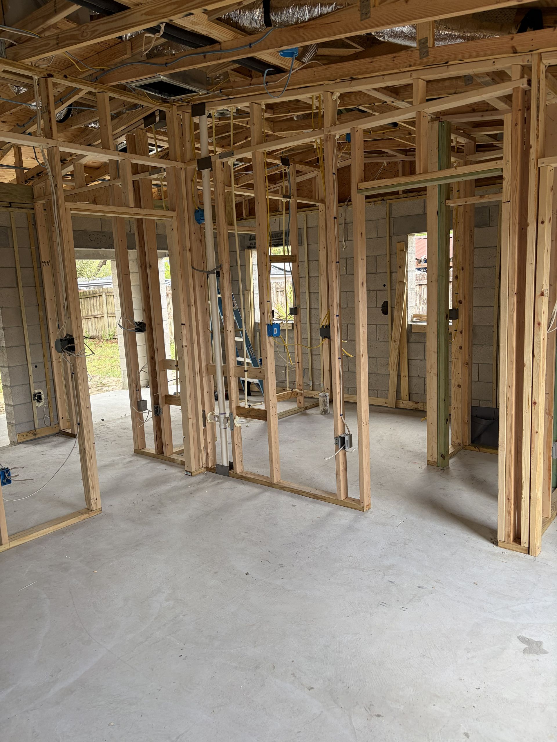 Unfinished house interior with exposed wooden framing, open doorways, and a bare concrete floor.