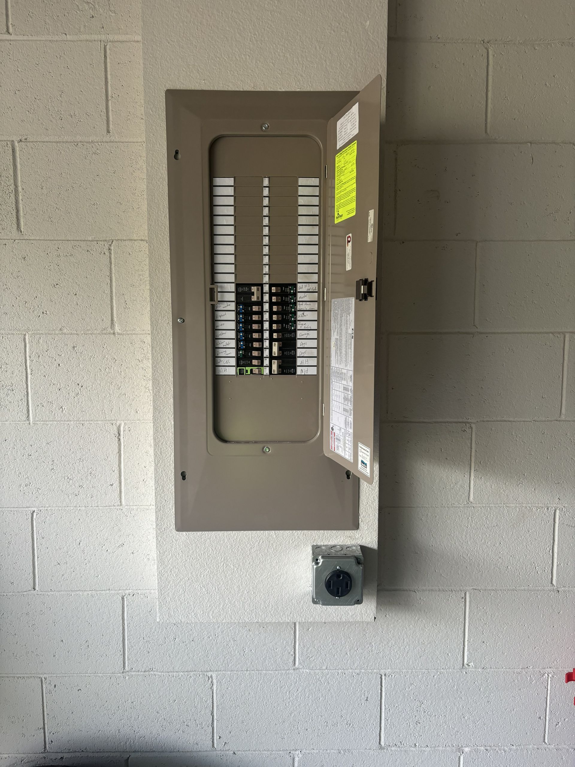 Open electrical breaker panel in a cinder block wall, door ajar.