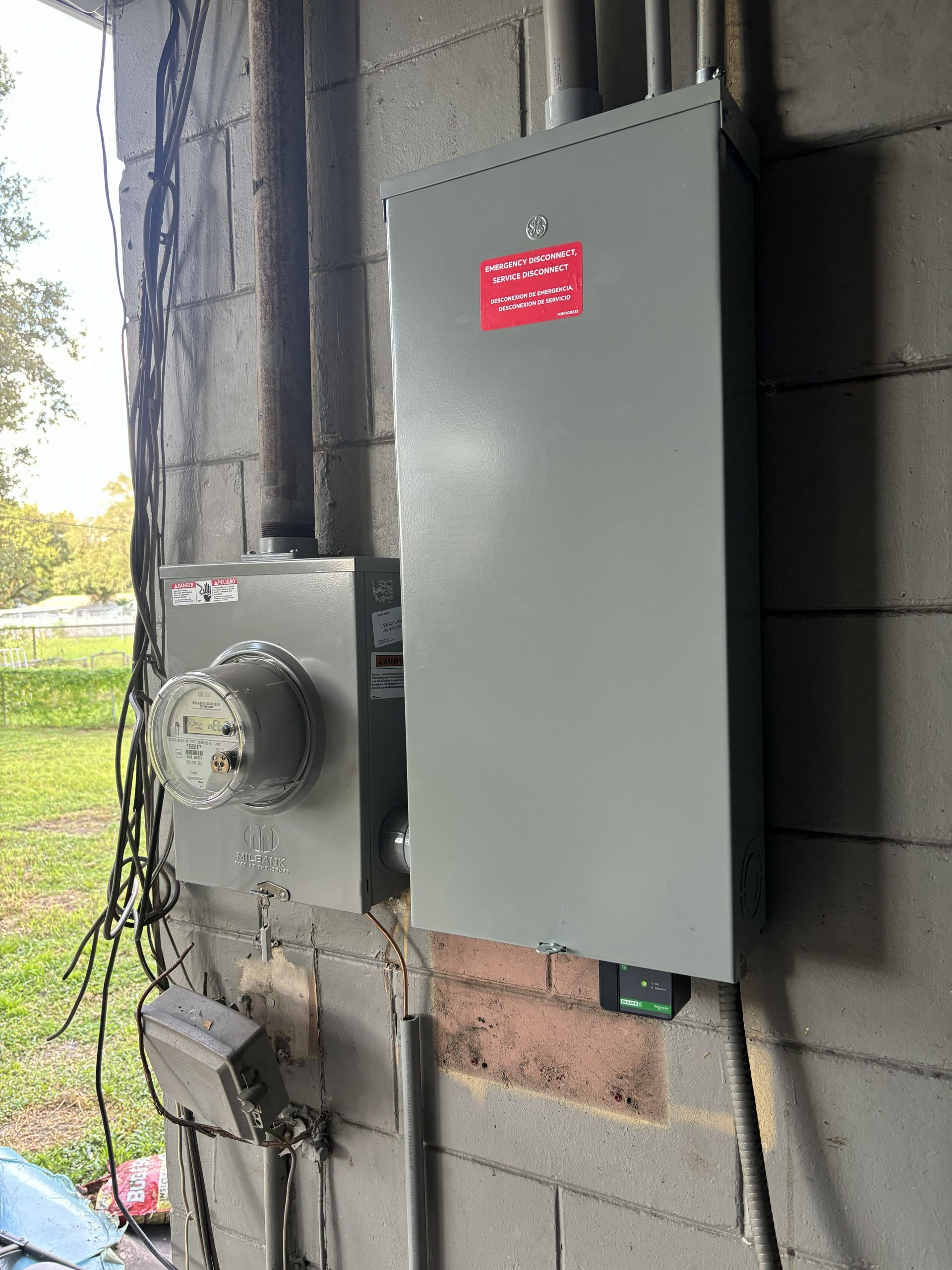Gray electrical panels and meters mounted on a cinder block wall outdoors
