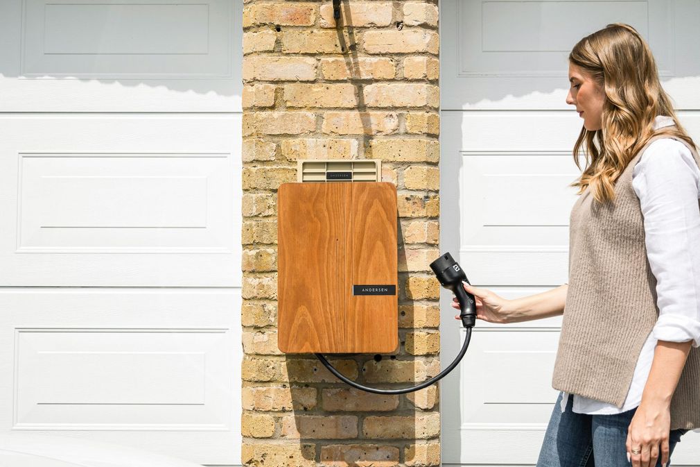 Woman charging an electric car at a wall-mounted home EV charger between two garage doors