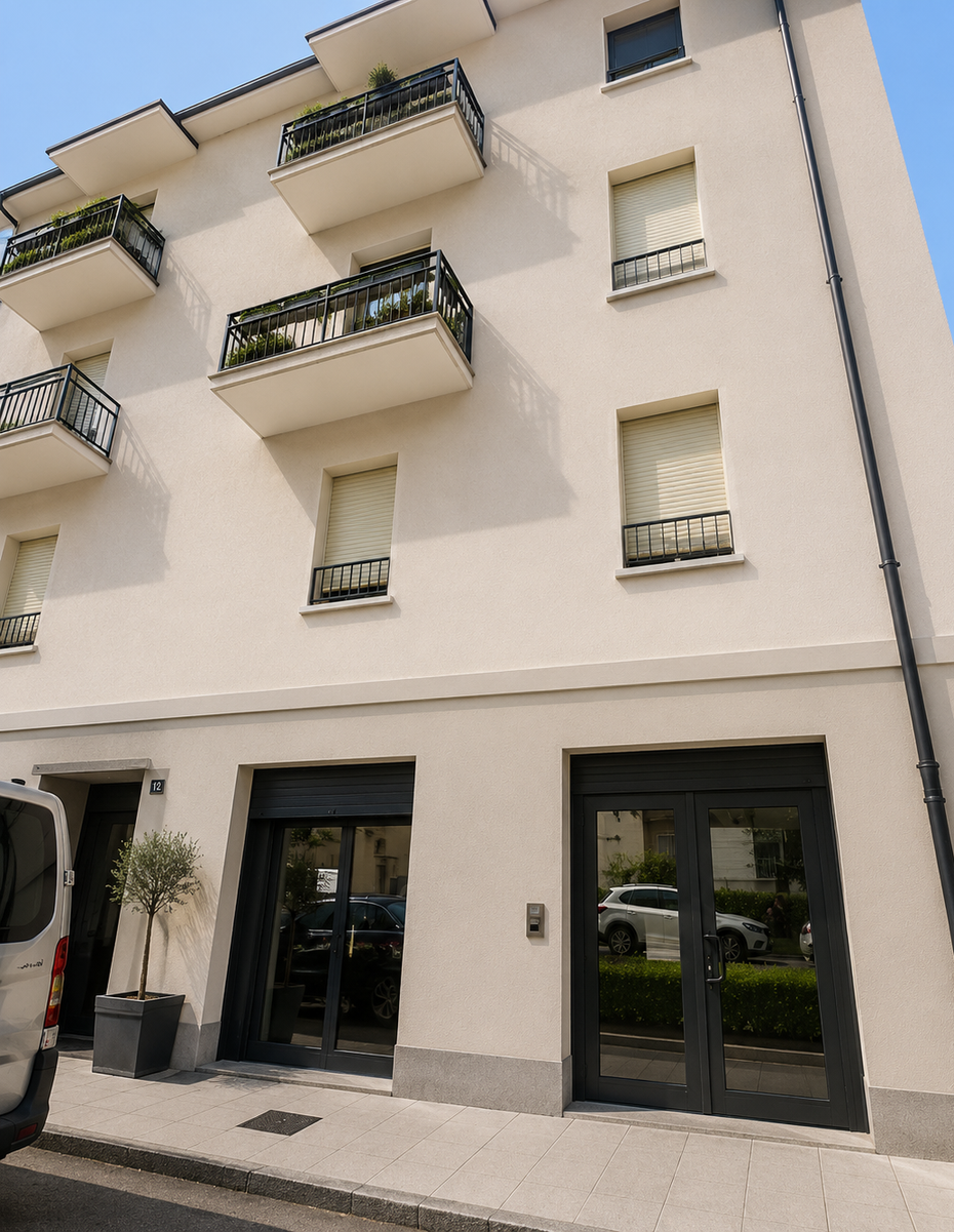Palazzo residenziale bianco con balconi e vetrine al piano terra, affacciato su una strada soleggiata.