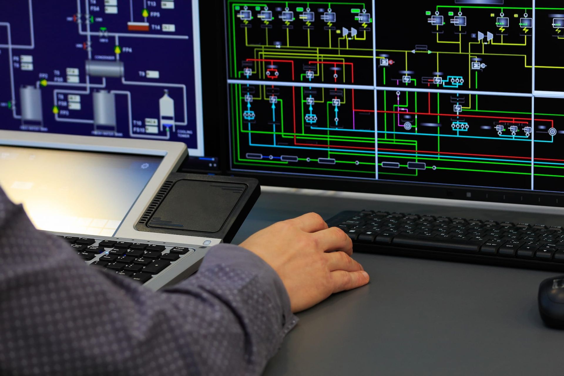 Person operating control panel with multiple screens displaying diagrams and data.