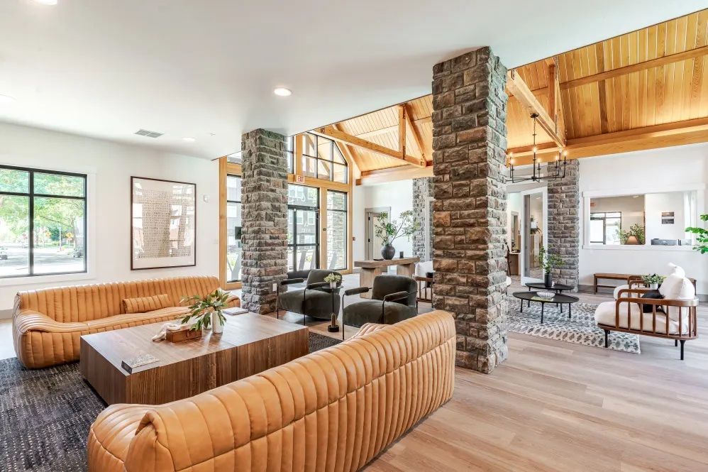 Spacious lounge with brown leather sofas, stone columns, and wooden beams.
