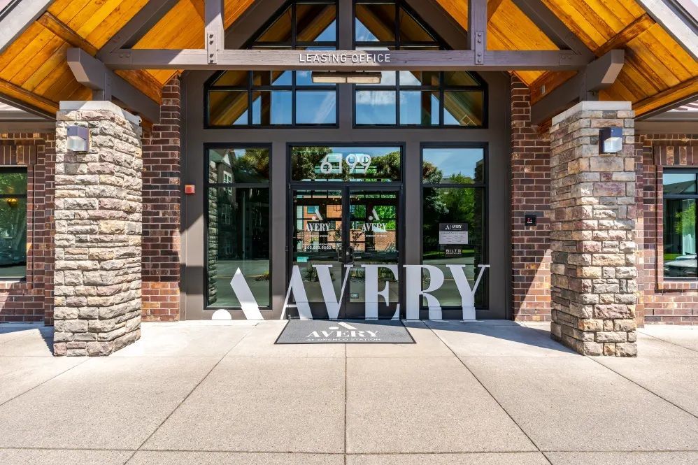 Entrance to Avery apartments with stone columns, glass doors, and wooden beams.