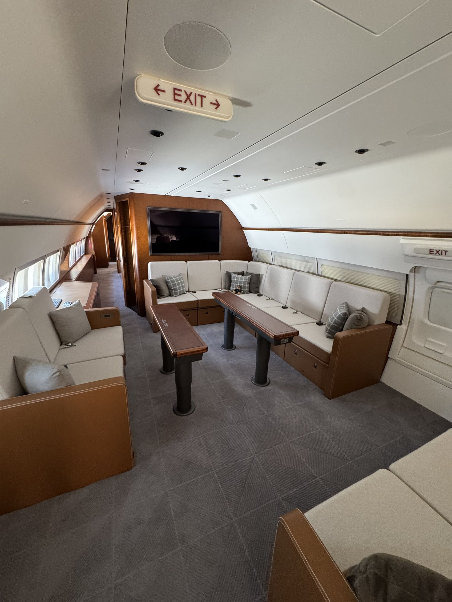 Private jet cabin with cream leather seating, wood accents, and central tables under an EXIT sign